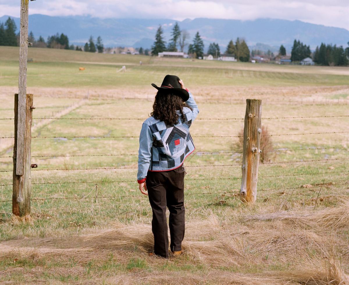 person with long hair in a field with a cowboy hat; focus is on the jacket which is quilted